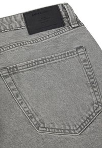 Los jeans de denim gris presentan un bolsillo trasero con costuras reforzadas y un parche de cuero negro en la cintura. Textura suave y ajuste entallado.