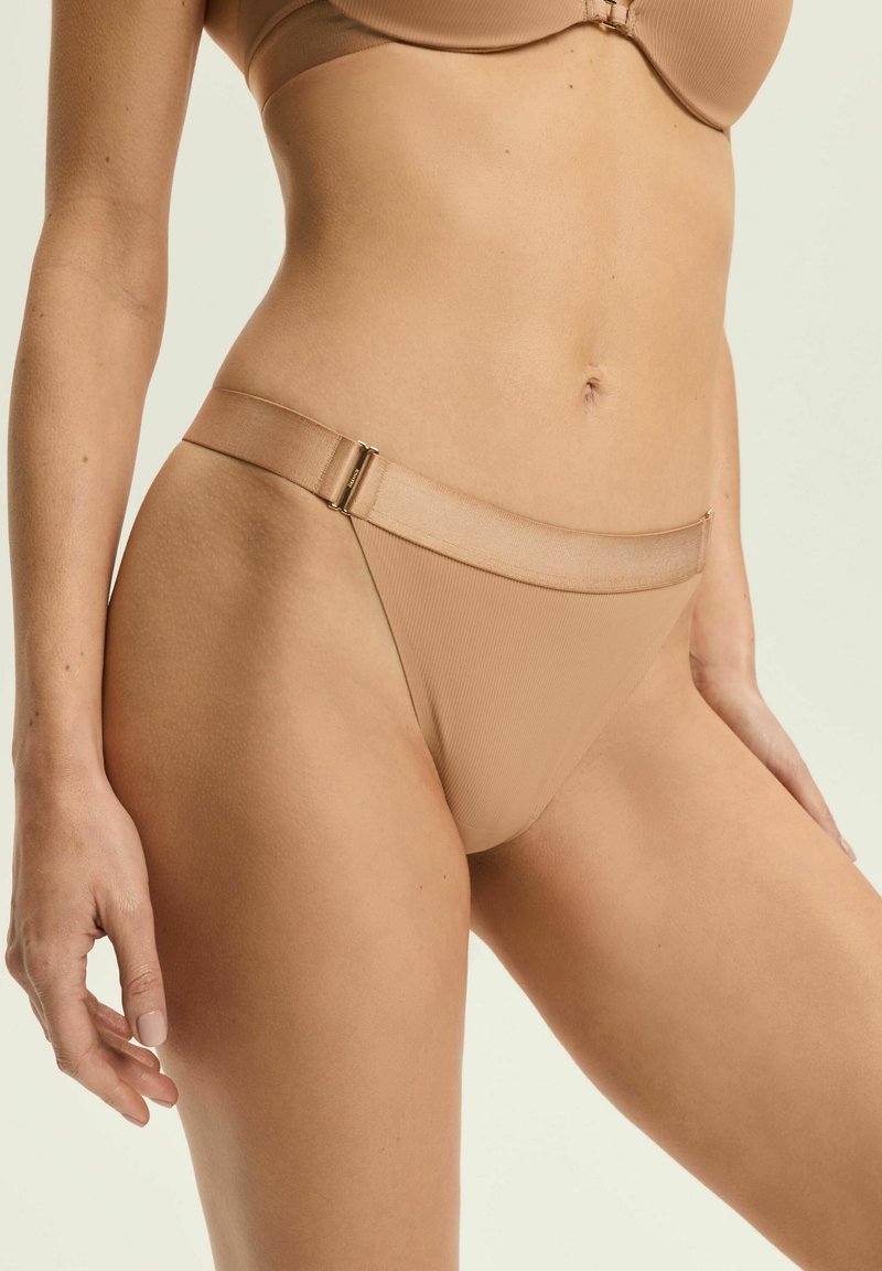 Beige gerippte Bikinihose mit breitem Bund und goldfarbenen Hardware-Akzenten. Glatte Textur und Design mit minimaler Abdeckung.