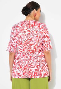 Camisa de manga corta roja y blanca con un estampado de hojas. La camisa tiene un corte holgado y un dobladillo curvado, combinada con pantalones verdes.
