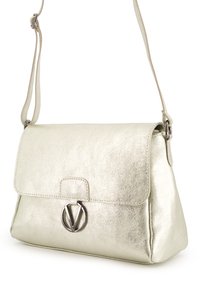 Srebrna torebka o metalicznym wykończeniu w prostokątnym kształcie, z płaską klapą, przeszywaną krawędzią oraz okrągłym akcentem w postaci logo. Regulowany pasek na ramię.