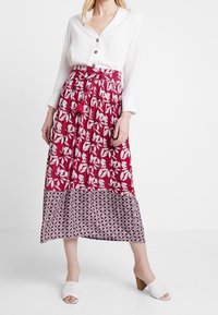 Rød blomsterprintet maxiskirt med en kontrasterende mønstret kant, parret med en hvid skjorte med knapper og hvide åbne mules.