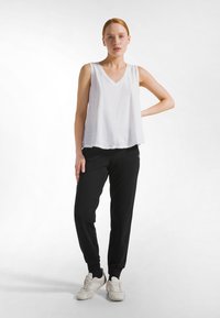 Top blanco sin mangas con escote en V y ajuste holgado, combinado con pantalones jogger negros y zapatillas grises claras. Ropa deportiva simple y casual.
