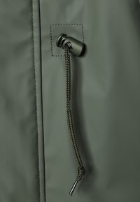 Tissu vert avec couture piquée présentant un verrou de cordon réglable vert et un cordon tressé avec embout métallique pendu.