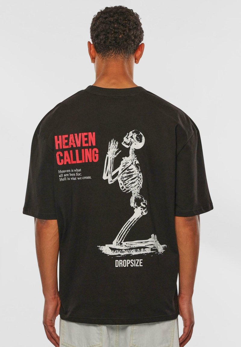 Sort oversized t-shirt med en hvid skeletgrafik og rød tekst "HEAVEN CALLING" på ryggen. I bomuldsstof, kortærmet.