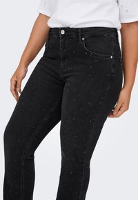 Melna džinsa bikses ar pieguļošu siluetu, dekorētas ar izkaisītiem rhinestone akcentiem un klasisku piecu kabatu dizainu. Metāla pogas aizdare.