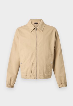 Beżowa kurtka zapinana na zamek z ostrym kołnierzem, bocznymi kieszeniami na zatrzaski, elastycznymi mankietami i elastycznym dołem na jednolitym tle.