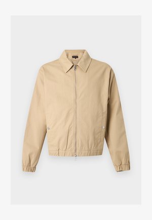 Beżowa kurtka zapinana na zamek z ostrym kołnierzem, bocznymi kieszeniami na zatrzaski, elastycznymi mankietami i elastycznym dołem na jednolitym tle.