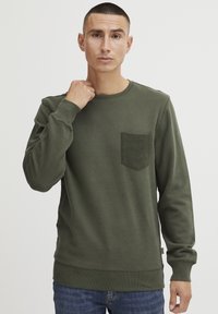 Oliven grønn genser i bomullsblanding, med en teksturert lomme, rund hals, ribbestrikkede ermer og hem. Enkel, uformell design.