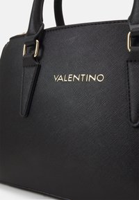 Svart texturerad handväska med släta läderdetaljer och guldtonad "Valentino"-logotyp, med två stabila handtag.
