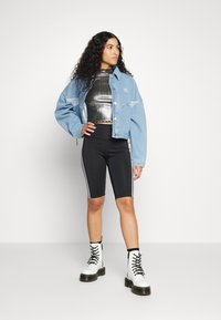 Veste en denim bleu clair, crop top noir métallisé, shorts de vélo noirs avec des rayures blanches sur le côté, et bottes de combat blanches à lacets.