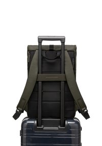 Sac à dos bicolore en tissu vert olive rembourré avec des accents noirs, monté sur une valise rigide bleue avec une poignée rétractable.