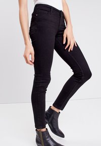 Mustat skinny-farkut, joissa on tyylikäs istuvuus, varustettuna tavallisilla taskuilla ja hienovaraisilla ompelu yksityiskohdilla, yhdistettynä nilkkabootseihin.