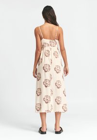 Maxi šaty krémové barvy s květinovým vzorem, tenkými ramínky, nařaseným zadním dílem a lehkým střihem, doplněné černými plochými sandály.