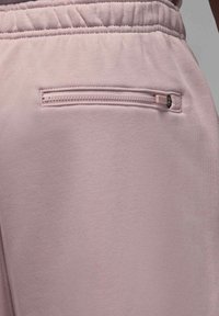 Lähikuva vaaleanvioleteista housuista, joissa on joustava vyötärö ja vaakasuora vetoketjutasku takana oikealla puolella.