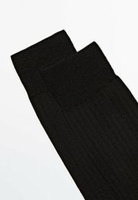 Sorte ribbede leggings med en struktureret overflade og en bred talje. Materialet ser strækbart og tætsiddende ud for komfort og varme.