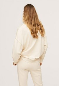 Sudadera de color crema, de corte holgado con hombros caídos, detalles de puños acanalados y pantalones jogger a juego de color crema. Textura de tela suave.