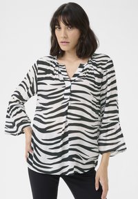 Blusa a righe bianche e nere con scollatura a V, maniche a campana tre quarti e tessuto leggero. Decorata con dettagli arricciati sul colletto.