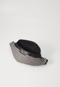 Borsa geometrica diagonale in bianco e nero con apertura a zip e un accento in pelle, caratterizzata da un logo metallico. Design texturizzato e compatto.
