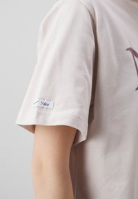 Primer plano de una persona que lleva una camiseta Nike de manga corta color beige claro con una pequeña etiqueta de Nike en la manga.