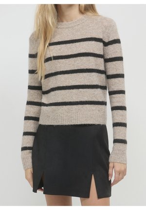 Femme portant un pull beige à rayures horizontales noires, associé à une mini-jupe noire avec des fentes à l'avant.
