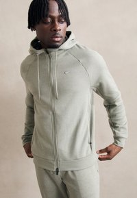 Lysegrøn zip-up hættetrøje lavet af blødt stof med snoretræk i hætten, der har et lille broderet logo på brystet og ribbede manchetter.