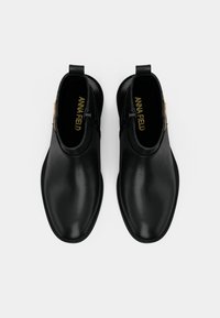 Botins de couro preto com uma textura suave, bico redondo e fecho lateral. Apresentam uma aba na parte de trás para fácil colocação. Nome da marca visível no interior.