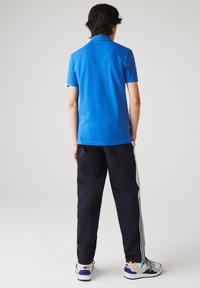 Niebieska koszulka polo, krótki rękaw, materiał bawełniany; zestawiona z ciemnogranatowymi spodniami z białymi paskami po bokach i białymi butami sportowymi.