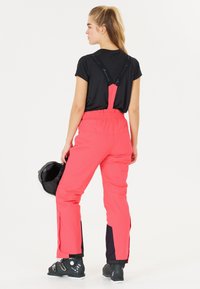 Roze skibroek met verstelbare bandjes, zwarte accenten bij de enkels en een relaxte pasvorm. Gekocht met een zwarte top en een zwarte helm in de hand.