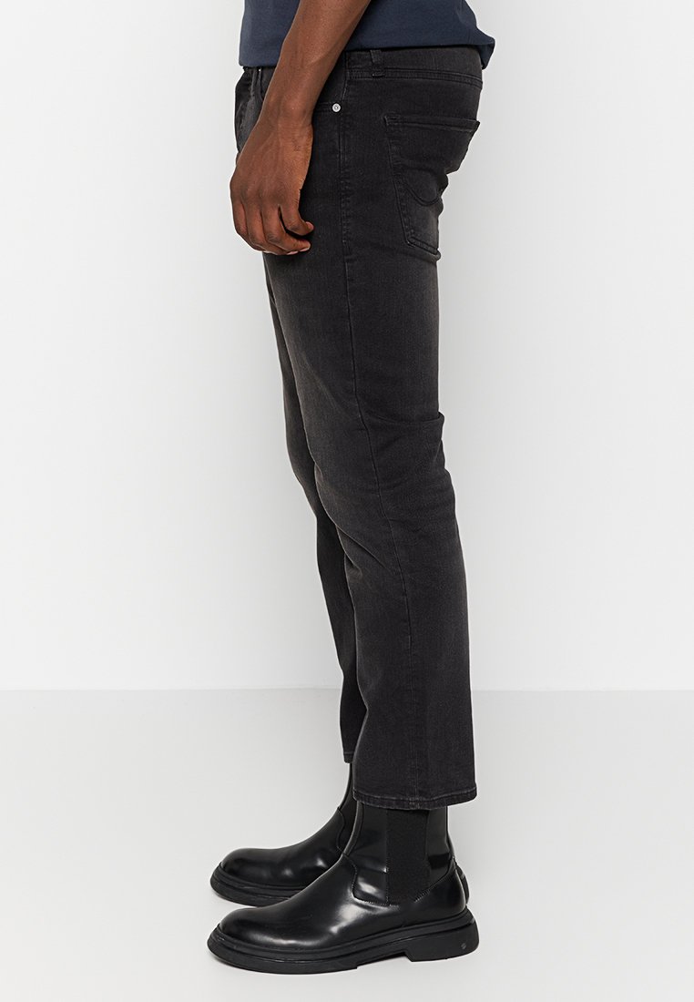 Schwarze Slim-Fit-Jeans aus Denim, mit fünf Taschen, einer glatten Textur und einem schmal zulaufenden Bein, kombiniert mit schwarzen Stiefeln.