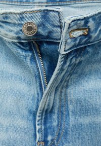 Farkut vaaleansinisellä pesulla, joissa on hopeinen nappisuljin, vetoketjullinen liepe ja kaksinkertainen tikkauksellinen reunus.