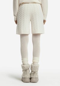 Vita stickade shorts med kabelmönster, kombinerade med vita leggings och fluffiga grå boots. Texturerad tyg och ribbade manschetter är synliga.