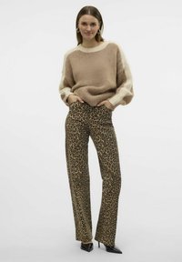 Un pull en tricot beige avec des coutures texturées et des accents crème, associé à un pantalon taille haute à imprimé léopard et des talons aiguilles noirs.