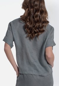 Lichtgrijze linnen shirt met korte opgerolde mouwen en een ontspannen pasvorm. Toon de achterkant, waarbij de zachte textuur en de val worden benadrukt.