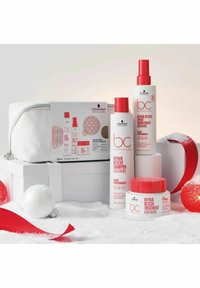 Schwarzkopf Bonacure Repair Rescue-setet innehåller schampo, balsam och behandling i vita och röda flaskor, uppställda på en vit låda med en påse.