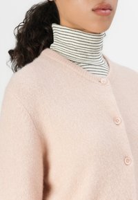 Light pink knitted cardigan with a V-neck and three buttons, layered over a black and white striped turtleneck. Soft texture, casual design.
