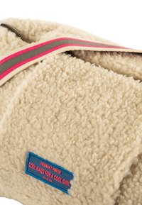 Manta de forro polar en color crema con una superficie texturizada. Cuenta con una banda de rayas coloridas y una etiqueta cosida en azul y rosa.