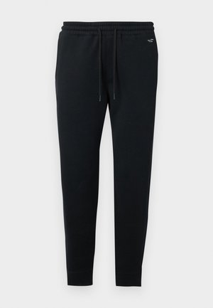 Pantalones de chándal negros fabricados con un tejido suave, que cuentan con una cintura elástica con cordón, piernas ajustadas y un pequeño logo en la parte superior izquierda.