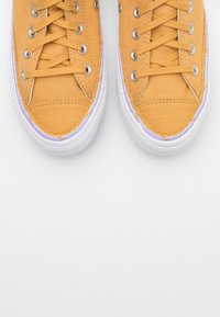 Płócienne trampki w jasnym żółtym kolorze z białymi gumowymi podeszwami i sznurowadłami. Posiadają srebrne oczka i teksturowany materiał.