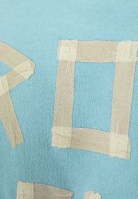 Tejido turquesa con una textura suave que presenta diseños en forma de cinta beige dispuestos en cuadrados y rectángulos.