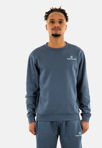 Sudadera de algodón azul con cuello redondo acanalado y mangas largas, que presenta el logotipo "Sergio Tacchini" bordado en el pecho.
