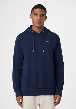 Un hombre luce una sudadera con capucha FILA azul marino, con cordones y un bolsillo delantero, sobre un fondo blanco liso.