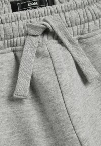 Pantalones de chándal grises con una superficie texturizada, cinturilla elástica y un detalle de cordón anudado. Tejido suave y cómodo con un corte holgado.