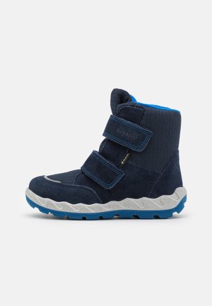 Bottes pour enfants bleu marine en suède et textile, avec deux bandes Velcro, un intérieur rembourré et une semelle texturée blanche et bleue.