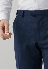 Námořnické modré kalhoty z texturované tkaniny s kostkovaným vzorem. Mají plochý přední díl a boční kapsy s hladkým pasem.
