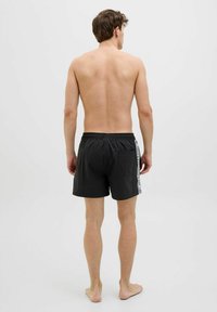 Zwarte zwemboxers met een elastische tailleband en een enkele achterzak. Zijkanten met contrasterende witte tekstdetails.