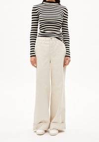 Haut à manches longues côtelé à rayures noires et blanches avec col haut, associé à un pantalon large crème et des baskets blanches.