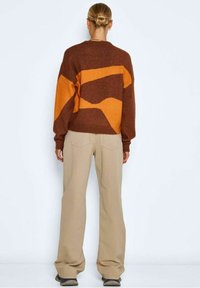 Brown and orange patterned sweater with a relaxed fit, paired with light beige wide-leg pants, shown from the back.