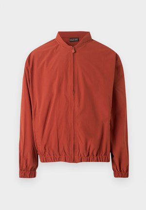 Ελαφρύ μπουφάν σε χρώμα σκουριάς με μπροστινό φερμουάρ, ελαστικές μανσέτες και ελαστική μέση, εμφανίζεται σε απλό φόντο.