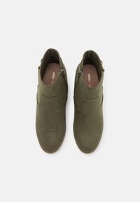 Bottines en daim vert olive avec une texture lisse, des fermetures éclair sur les côtés et une forme de bout arrondi. Semelle intérieure douce visible à l'intérieur.