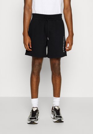 Man wearing black drawstring shorts with vertical white "Abercrombie" text, white crew socks, and black and silver running shoes.
